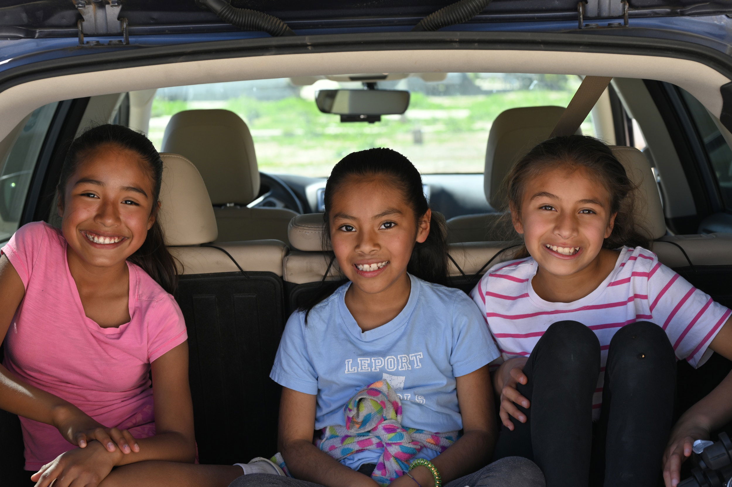 Children smiling and sitting in the back seat of the car