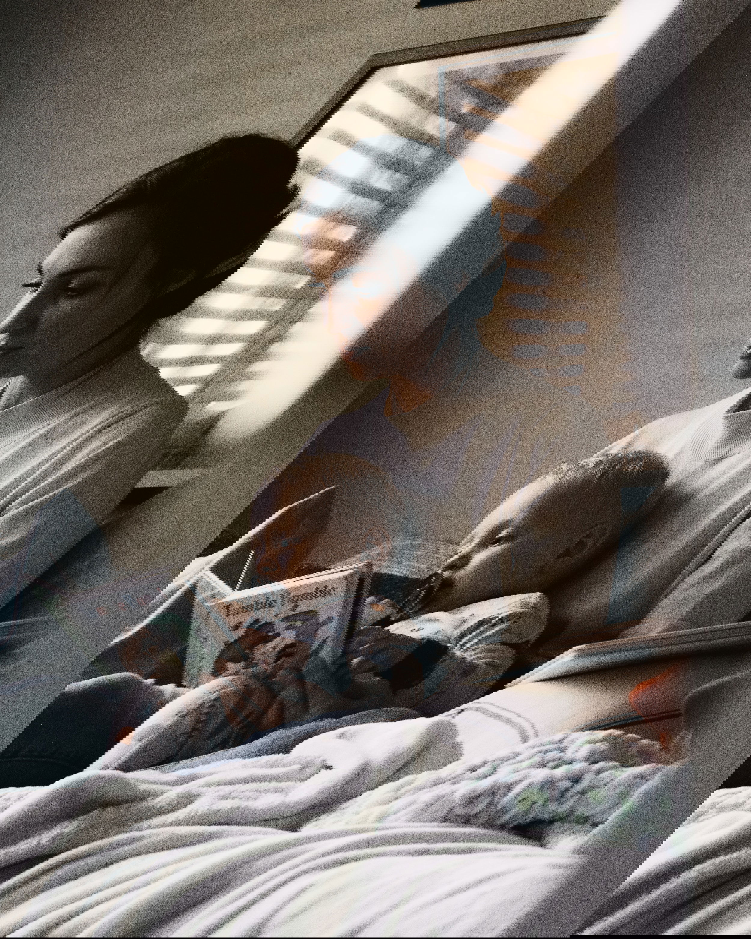 A toddler is reading books in the lap of his mother