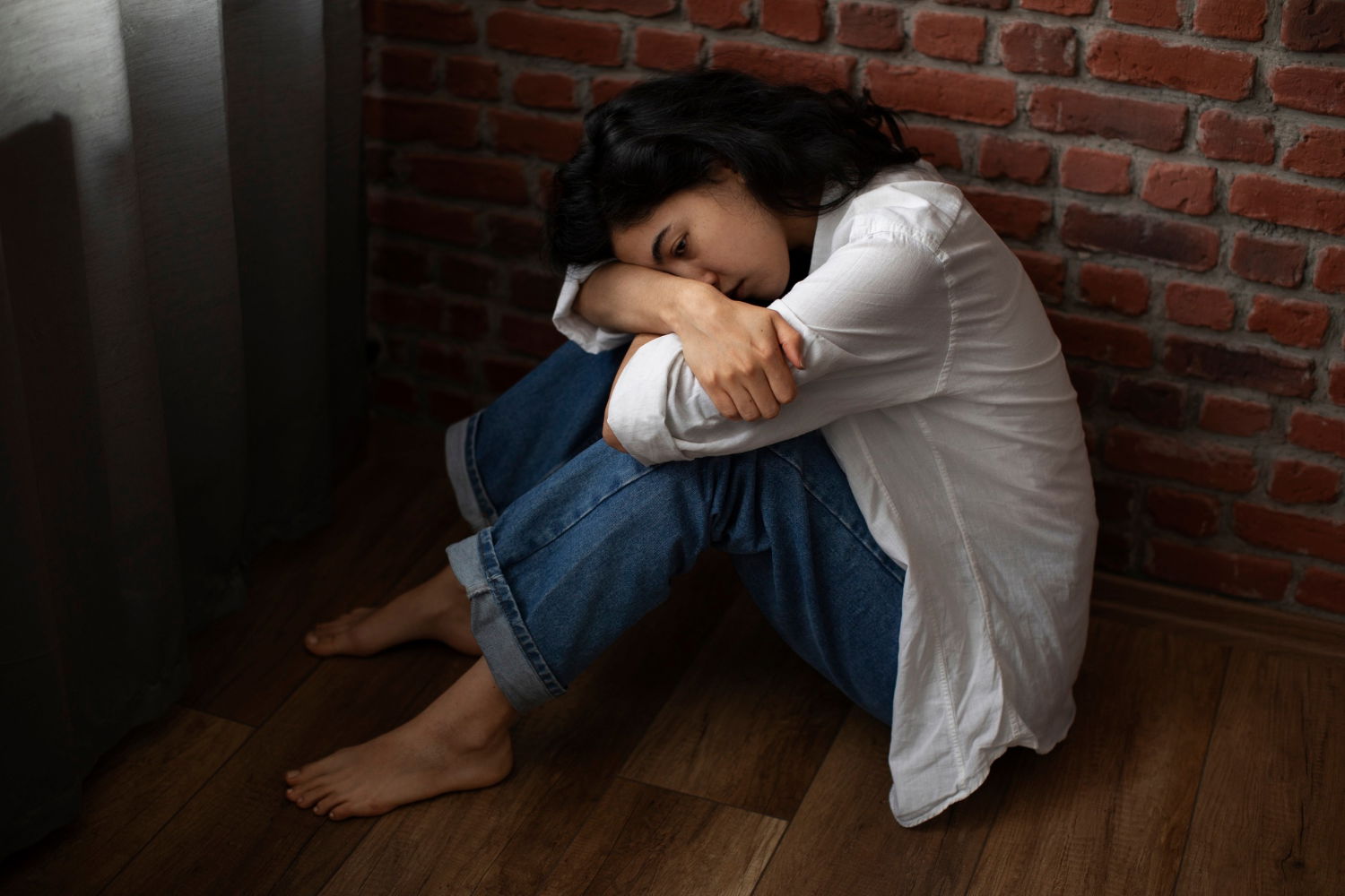 Young woman sitting on the floor with her head and arms on her drawn up knee