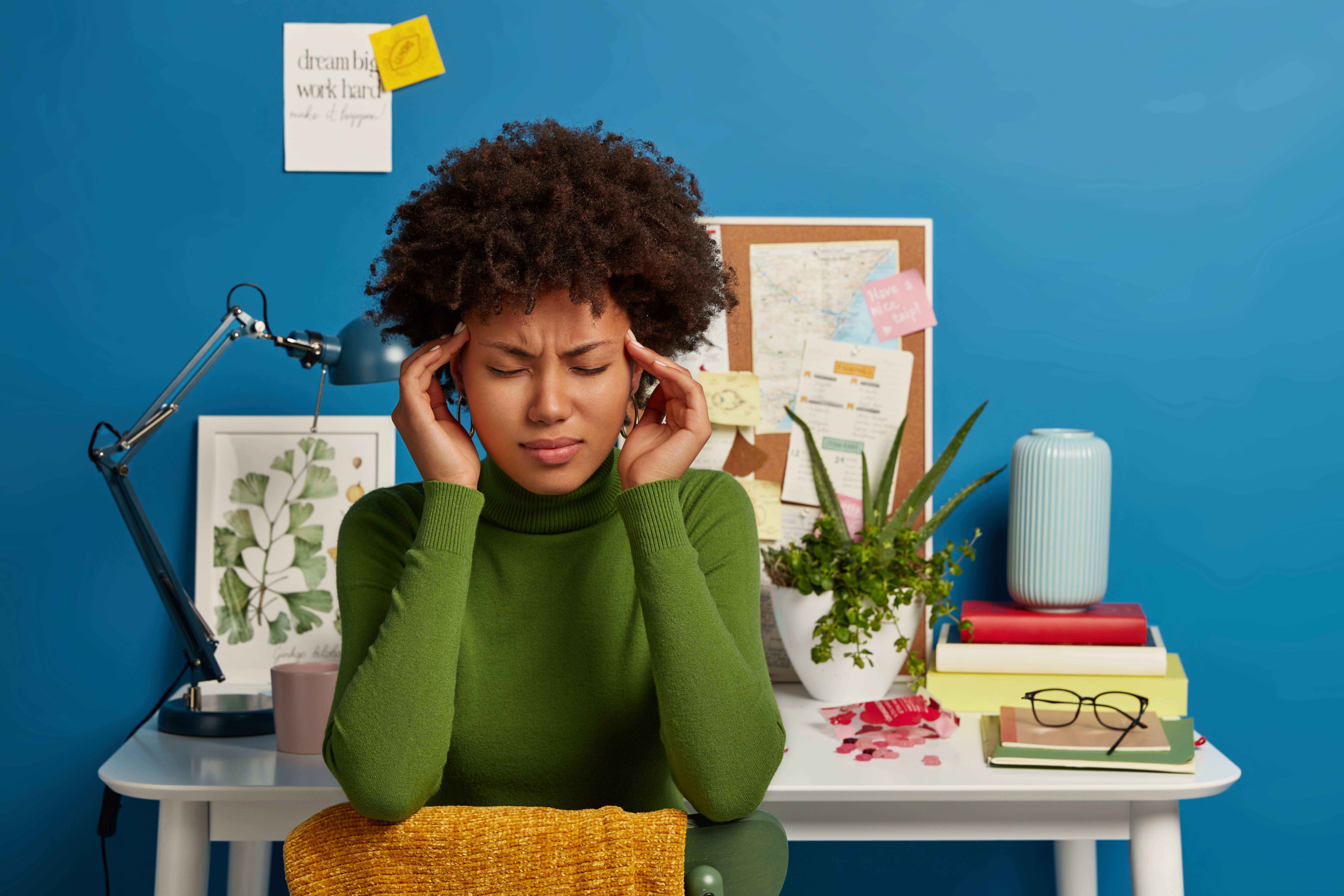 Upset, tired woman keeps both hands on temples, frowns, face, feels overworked after working long time
