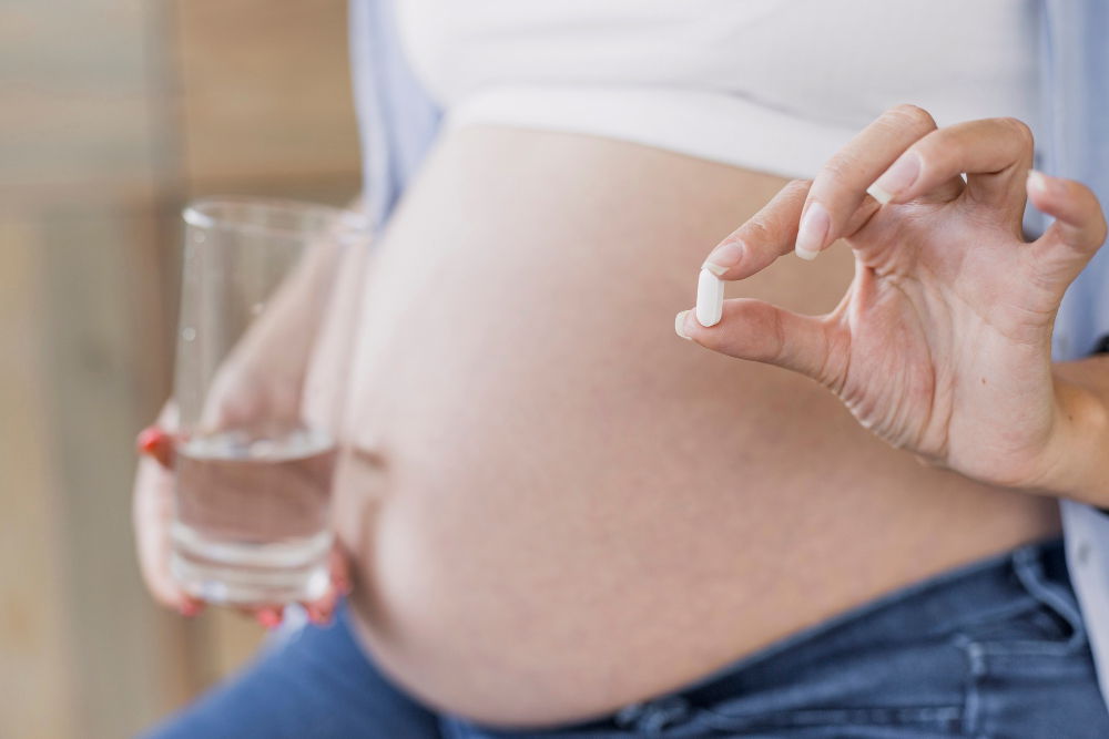 Pregnant woman holding a pill in one hand and a glass of water in the other.