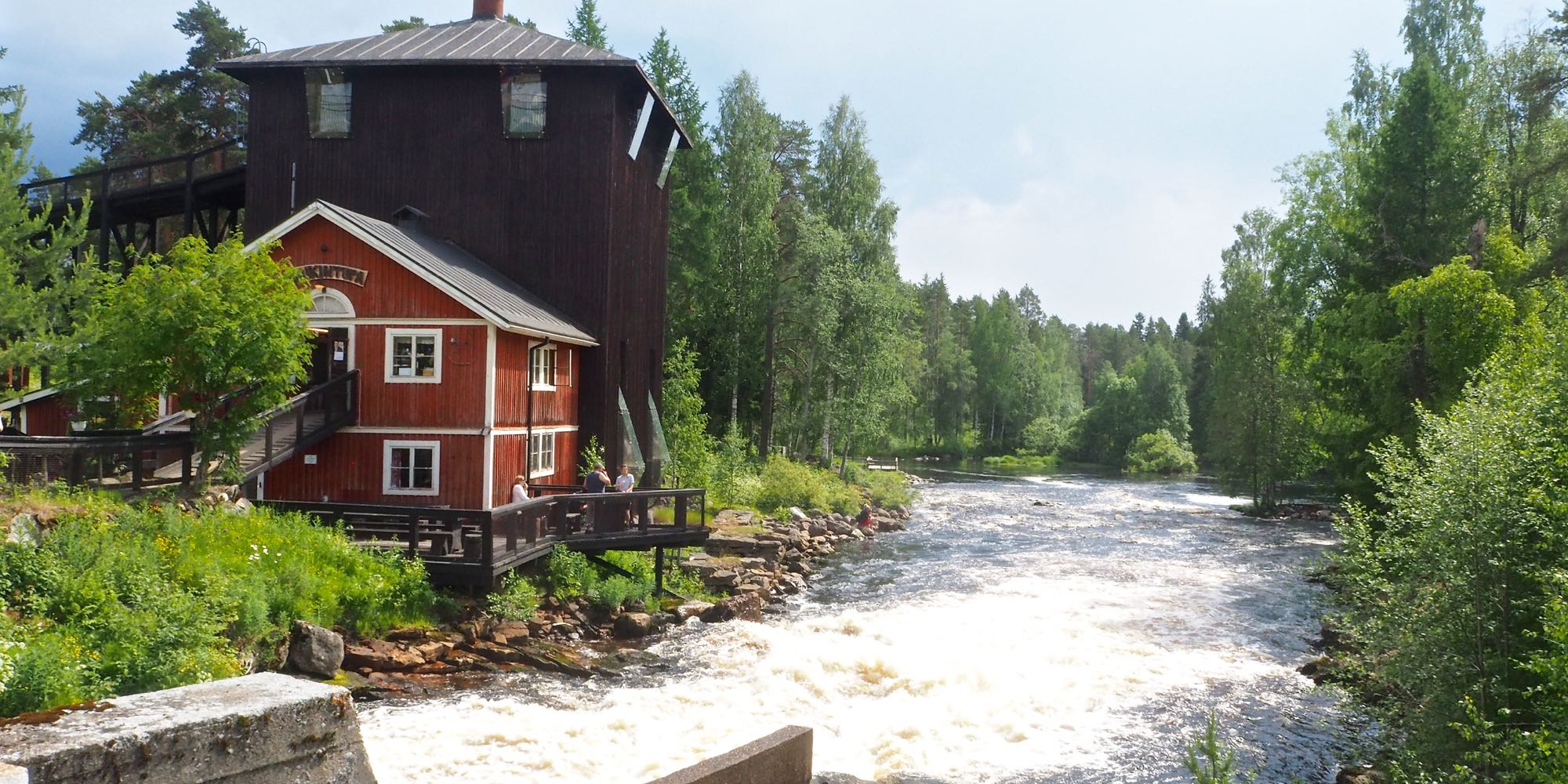 Punainen rakennus kuohuvan kosken rannalla.