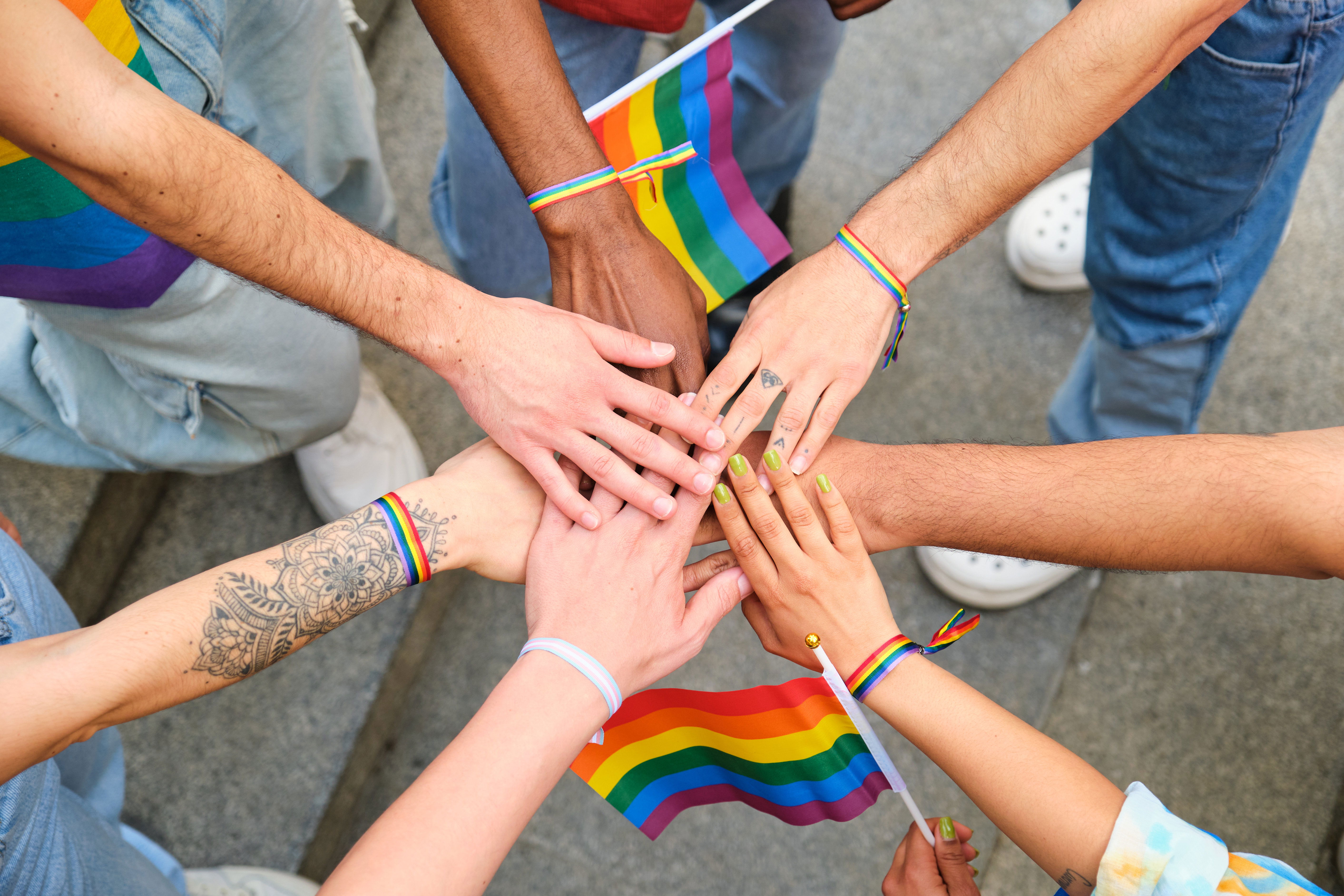 A group of friends hold hands around a rainbow flag, signaling solidarity with the LGBTQ community in recovery.