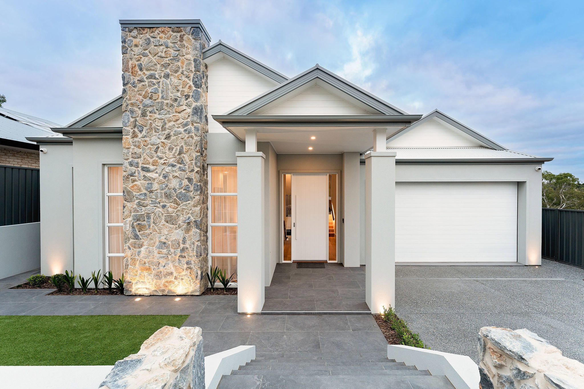 A modern house with a stylish stone pillar, sleek neutral walls, a grand entrance, and a spacious driveway leading to a double garage, showcasing knock down rebuild construction.