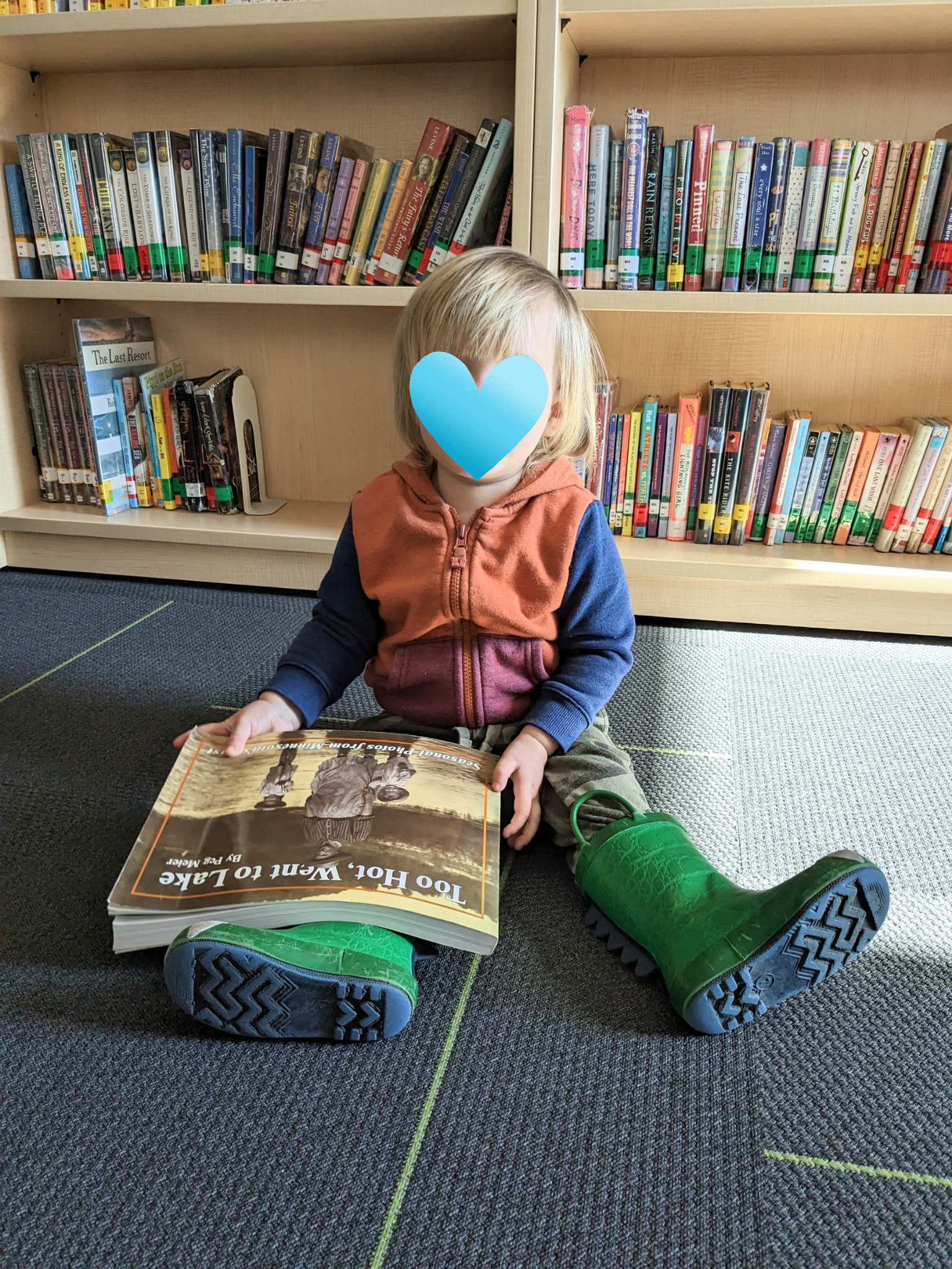 A little boy with his face protected is looking at a book at the library