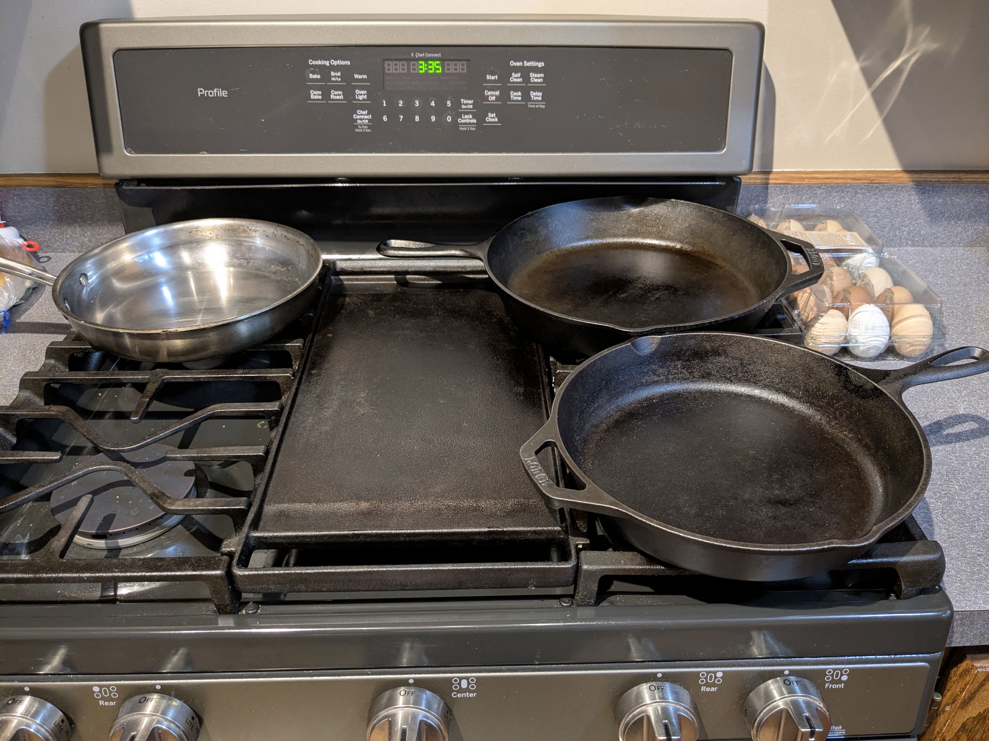 A cast iron stove features two different size cast iron pans and one stainless steel pan.