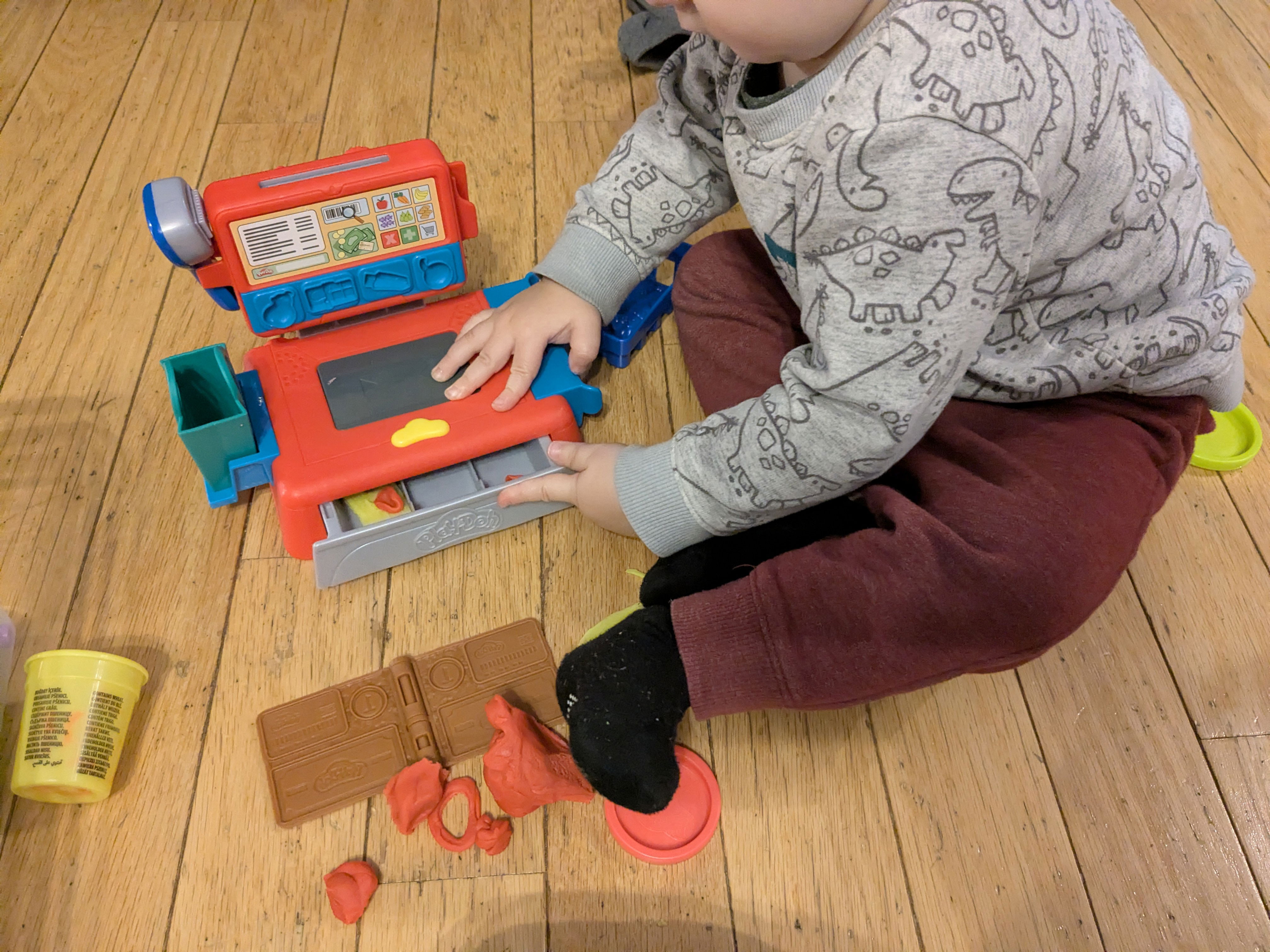 A baby playing with a cash register play doh set. 