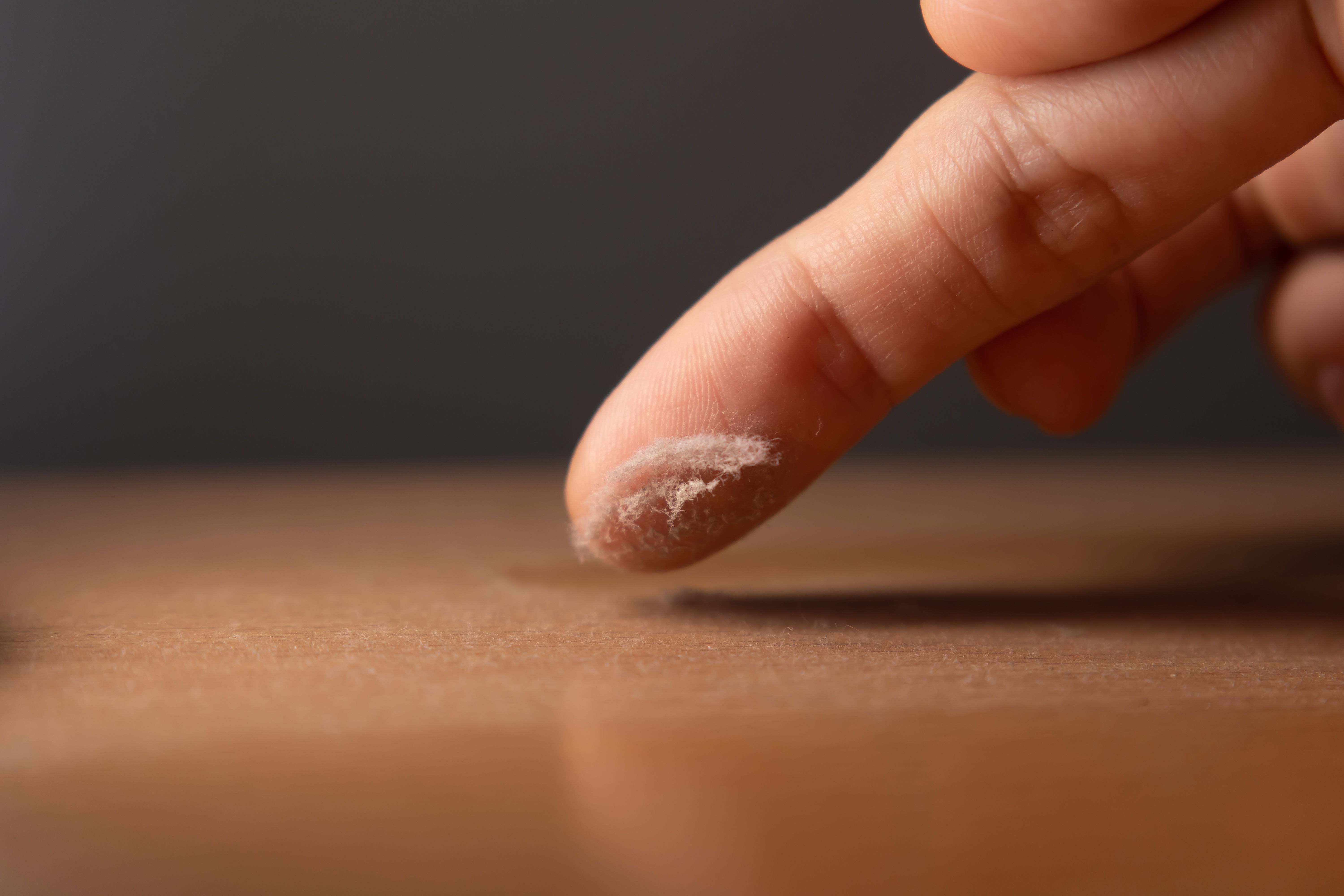 A photo of a finger picking up dust off the surface of furniture in a home