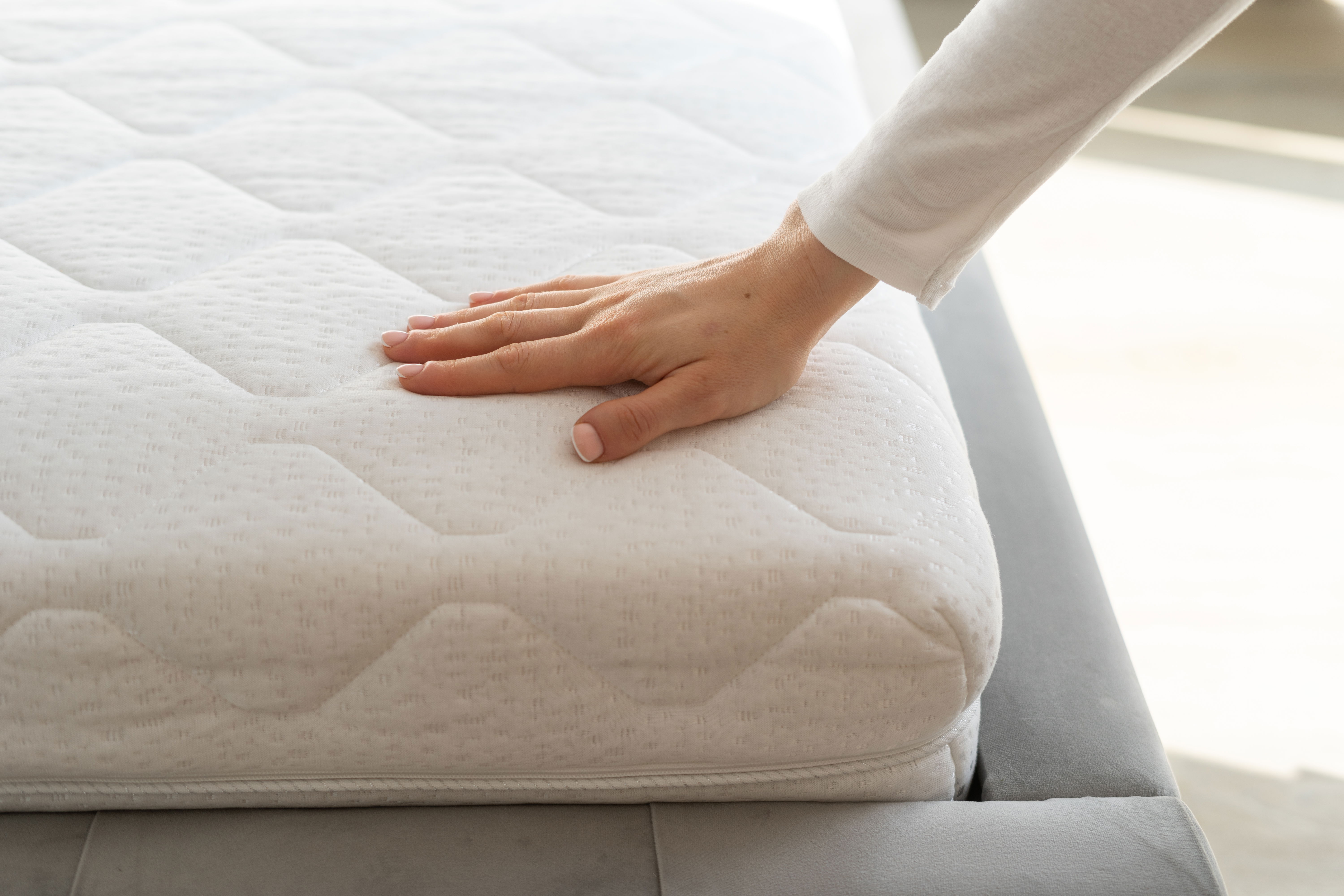 A photo of a woman's hand touching a white mattress