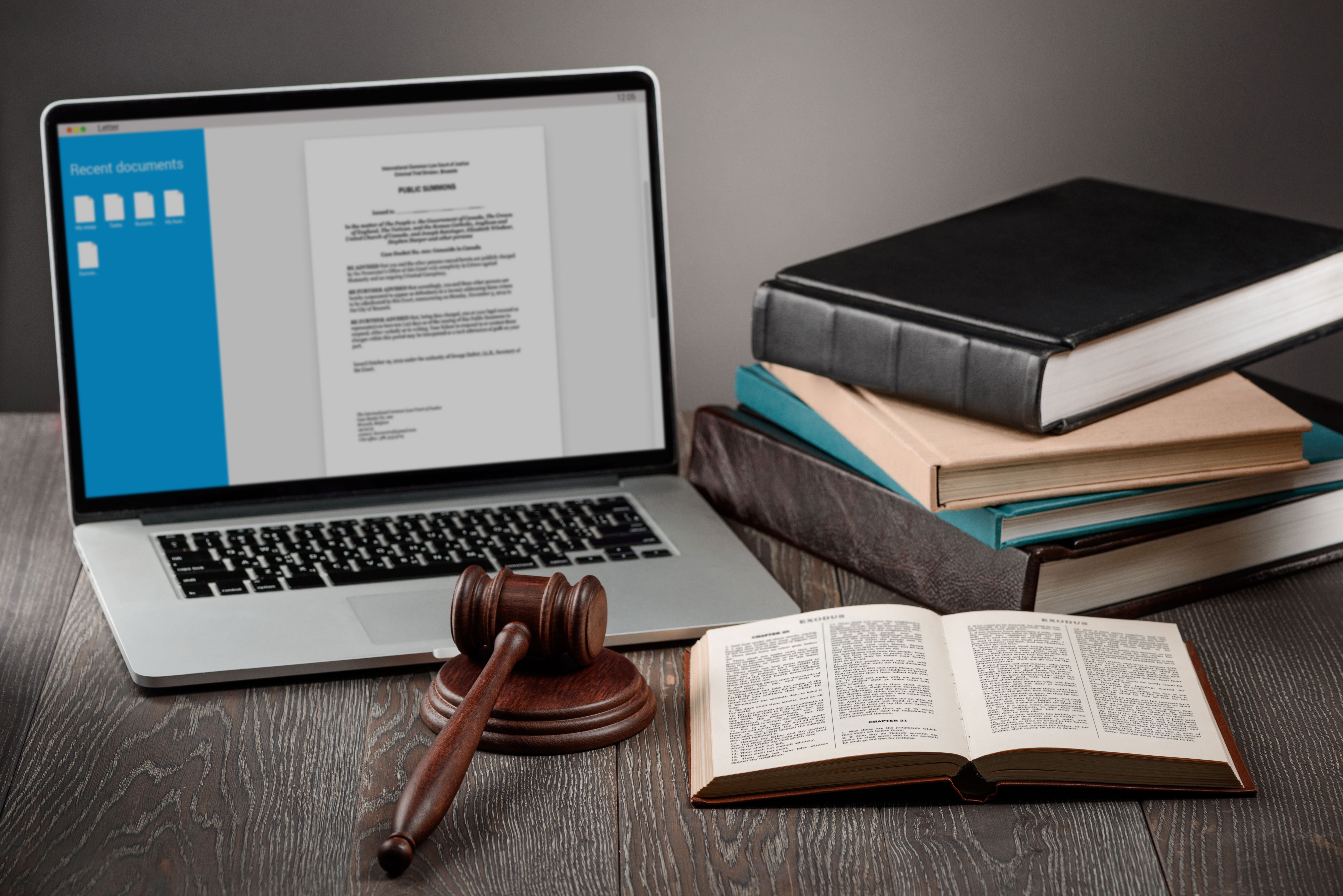 Books and a judge's gavel are shown surrounding an open lap top.