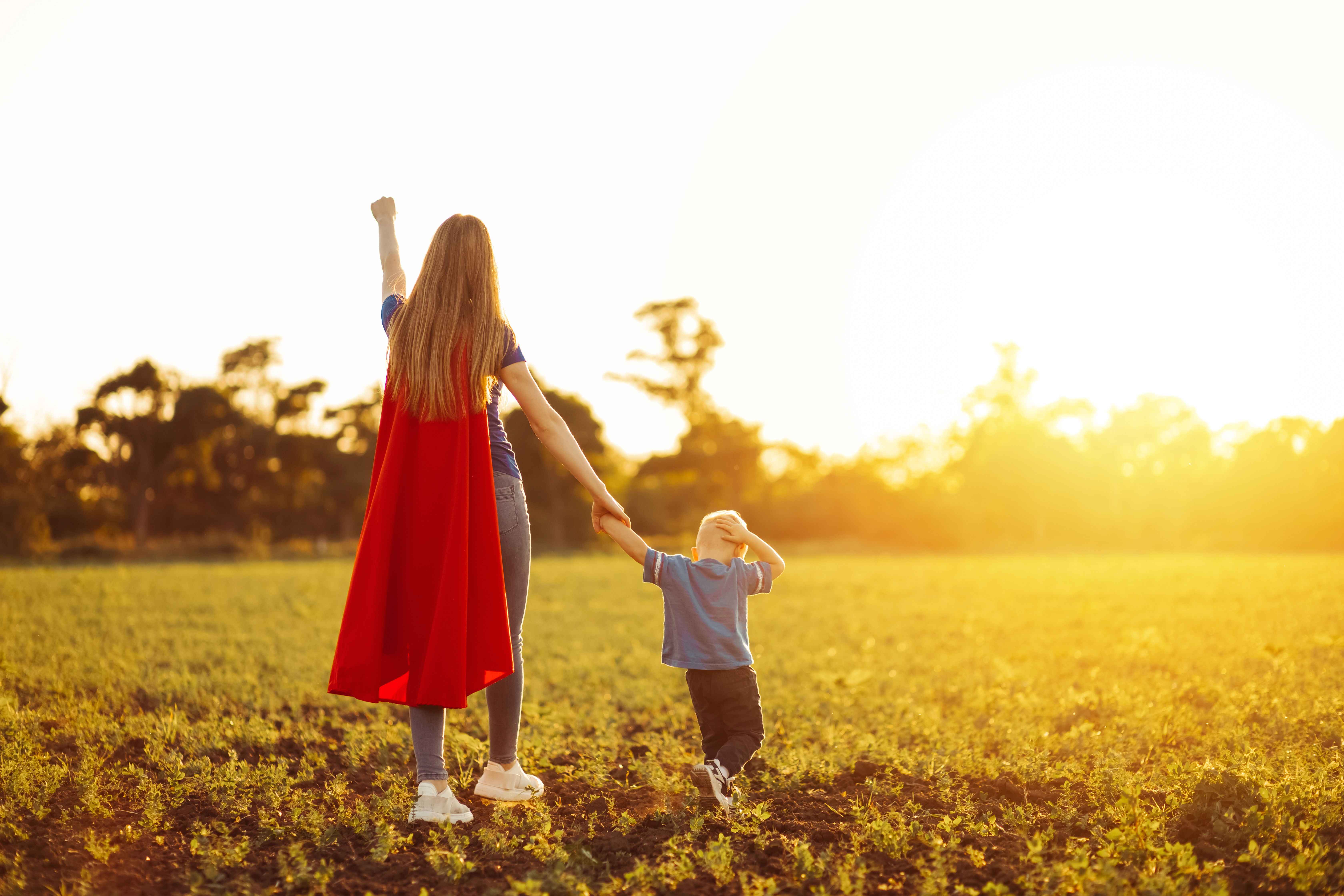 A woman and her son are shown from behind. The woman has her hand raised in the air and is wearing a super hero cape.