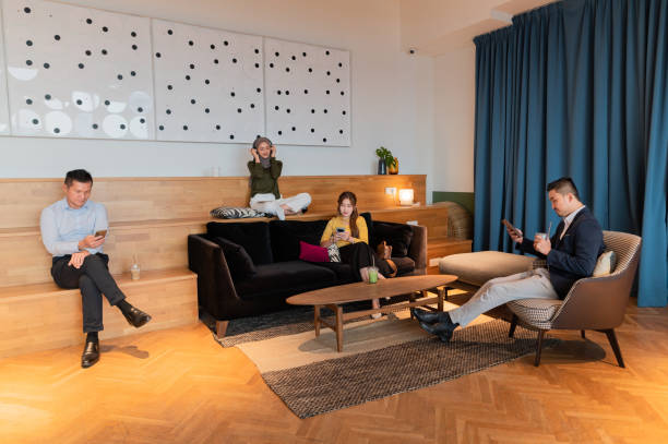 A group of individuals seated on couches in a coliving room, featuring a plain wall behind them.