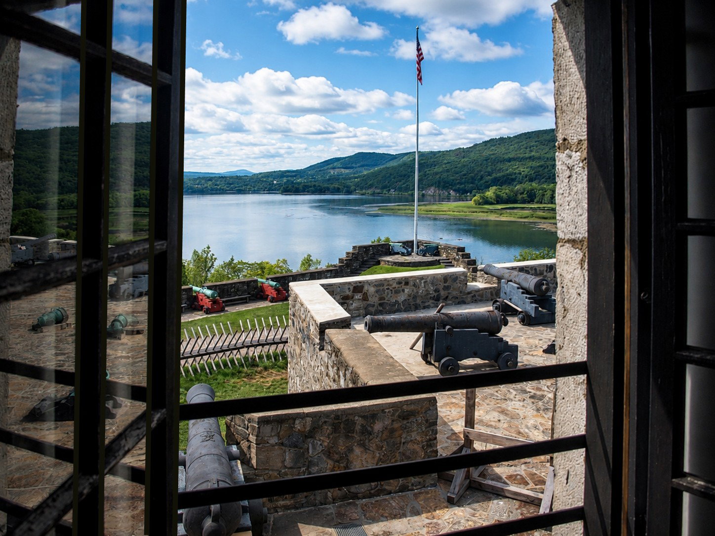 America 250: Lake Champlain and Fort Ticonderoga’s artillery defenses are seen through a window inside the fort in Ticonderoga, N.Y. The narrow Champlain Valley formed a natural invasion corridor between Canada and New York, making Ticonderoga one of the region’s most strategically important military positions during the 18th century. [Photo: S Cobaugh, Aug. 22, 2026]