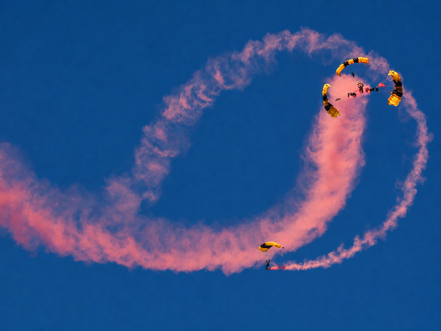 Members of the U.S. Army Golden Knights maneuver beneath their parachutes while trailing colored smoke during a precision aerial demonstration at the 100th Appalachian Fair in Gray, Tennessee. The Army’s official parachute team typically begins its full demonstration jumps from about 12,500 feet above the ground, using free-fall and canopy maneuvers to showcase precision skydiving skills before landing in the designated target area. [Photo: S Cobaugh, Aug. 27, 2026]