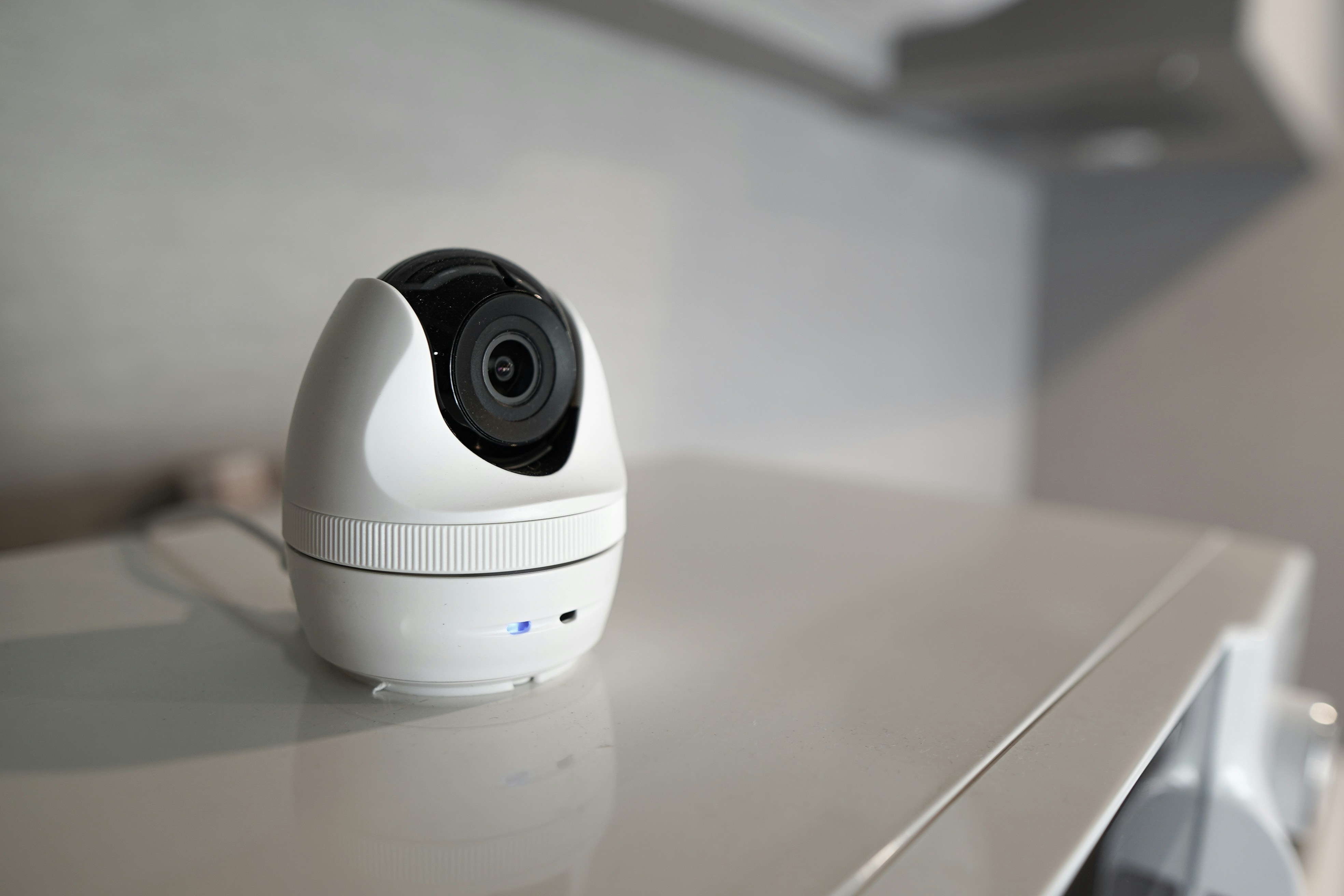 A small white, modern dome camera on a white surface indoors, illustrating a contemporary solution for discreet Nanny Cams Monitoring and indoor Home Surveillance.