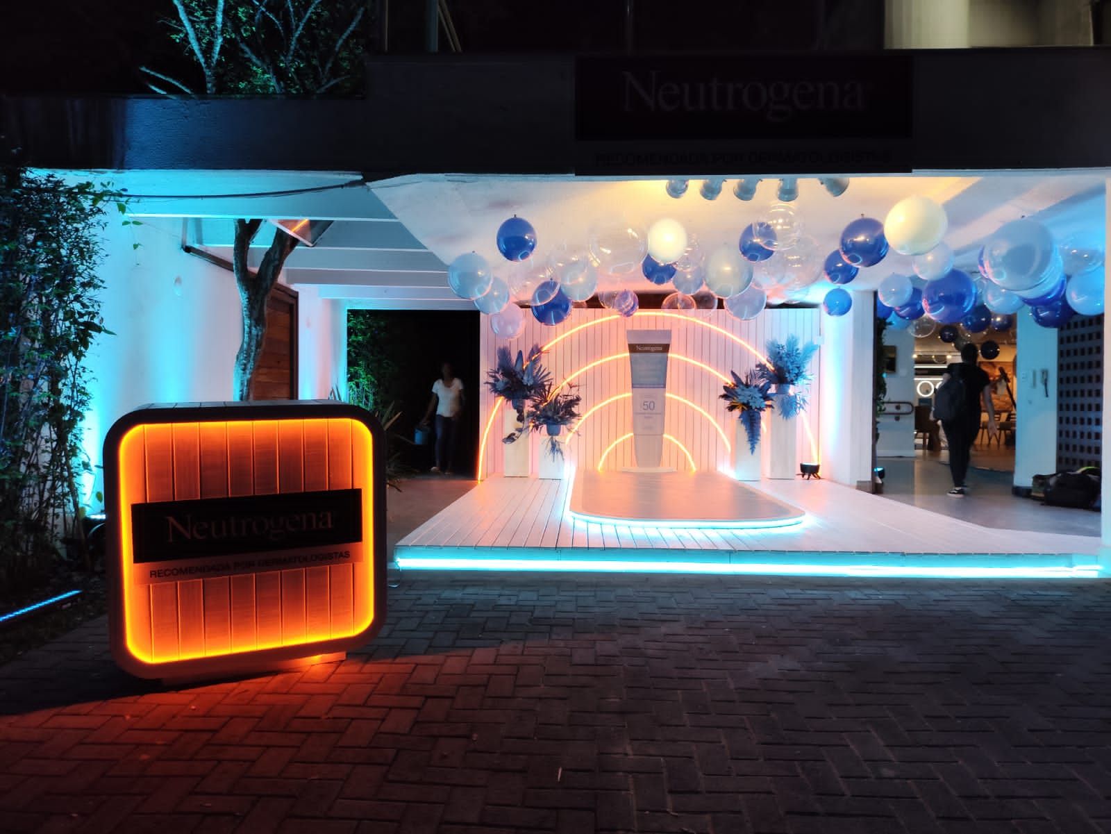 Cenografia imersiva da marca Neutrogena com estrutura iluminada em LED, balões decorativos e palco instagramável, montada pela Ari Cenografia para eventos de ativação noturna.