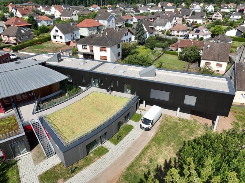 Charpente et murs à ossature bois - Couverture et bardage en zinc à joint debout - Etanchéité sur toiture terrasse avec protection par gravillons et végétalisation - Bardage en bois teinte sombre - Bardage en bois en sous-face - Bardage en Trespa®