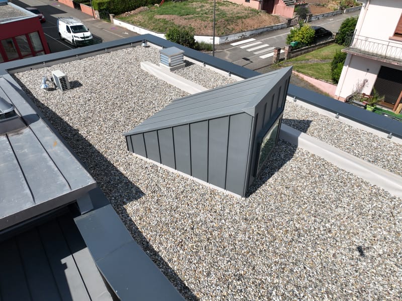 Charpente et murs à ossature bois - Couverture et bardage en zinc à joint debout - Etanchéité sur toiture terrasse avec protection par gravillons et végétalisation - Bardage en bois teinte sombre - Bardage en bois en sous-face - Bardage en Trespa®