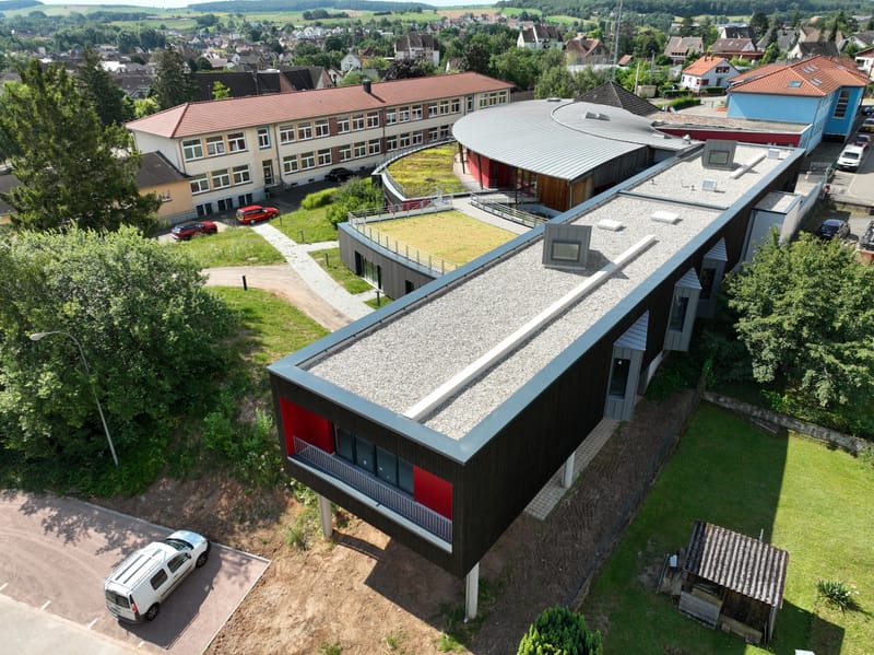 Charpente et murs à ossature bois - Couverture et bardage en zinc à joint debout - Etanchéité sur toiture terrasse avec protection par gravillons et végétalisation - Bardage en bois teinte sombre - Bardage en bois en sous-face - Bardage en Trespa®