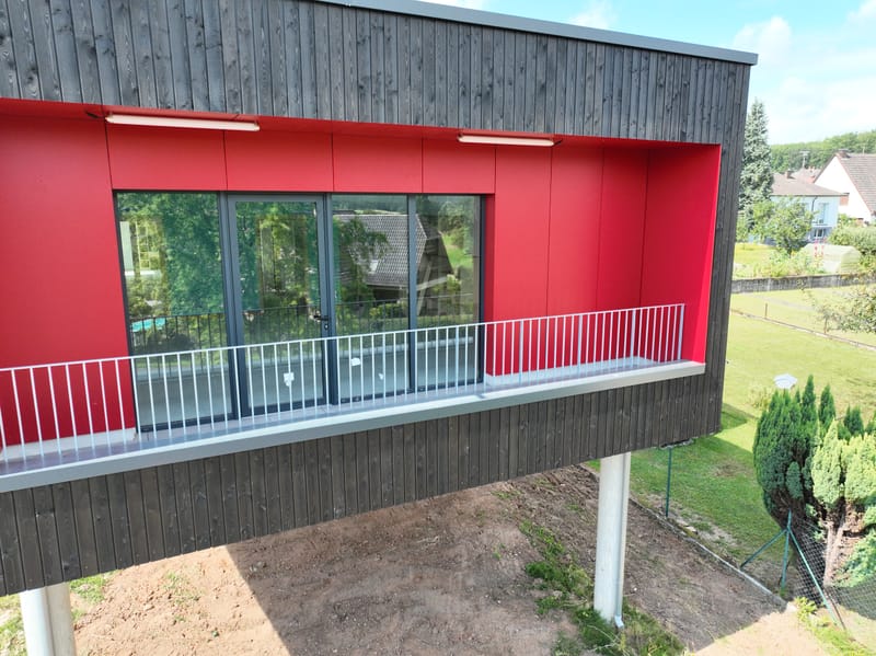 Charpente et murs à ossature bois - Couverture et bardage en zinc à joint debout - Etanchéité sur toiture terrasse avec protection par gravillons et végétalisation - Bardage en bois teinte sombre - Bardage en bois en sous-face - Bardage en Trespa®