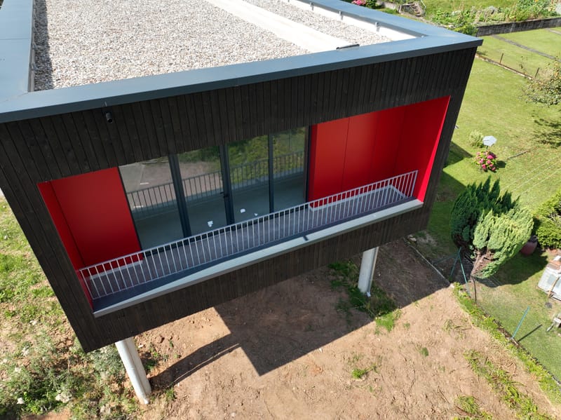 Charpente et murs à ossature bois - Couverture et bardage en zinc à joint debout - Etanchéité sur toiture terrasse avec protection par gravillons et végétalisation - Bardage en bois teinte sombre - Bardage en bois en sous-face - Bardage en Trespa®