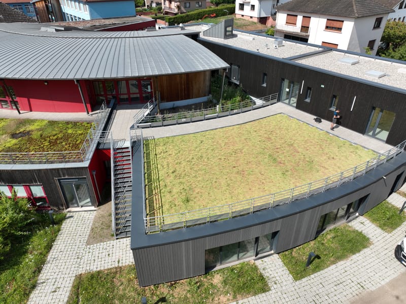 Charpente et murs à ossature bois - Couverture et bardage en zinc à joint debout - Etanchéité sur toiture terrasse avec protection par gravillons et végétalisation - Bardage en bois teinte sombre - Bardage en bois en sous-face - Bardage en Trespa®