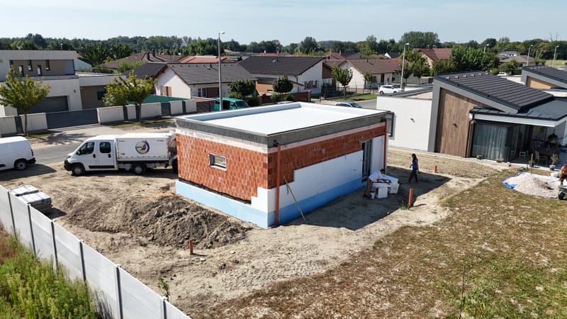 A képen a garázs homlokzatának hőszigetelési és festési munkálatai láthatók. A projekt során korszerű hőszigetelő anyagokat alkalmaztunk, majd esztétikus, időjárásálló kültéri bevonattal láttuk el a felületet, biztosítva a tartósságát.