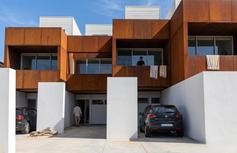 Façades en acier corten posés sur des murs de refend en béton blanc, surmonté d'un attique en bardage bois blanc