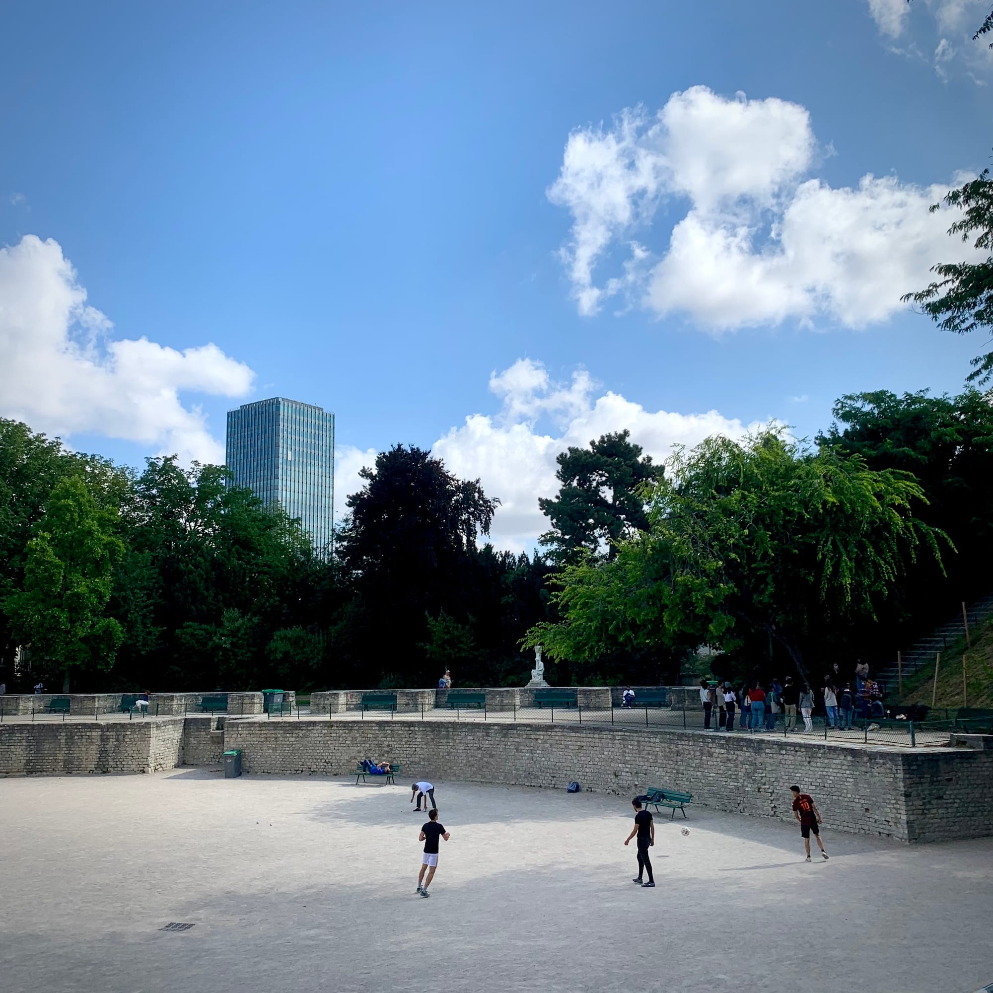 Vue sur les arènes de Lutèce : des enfants jouent au football dans les arènes, le ciel est bleu et agréable. À l'arrière plan : la tour Zamanski du campus de Jussieu.