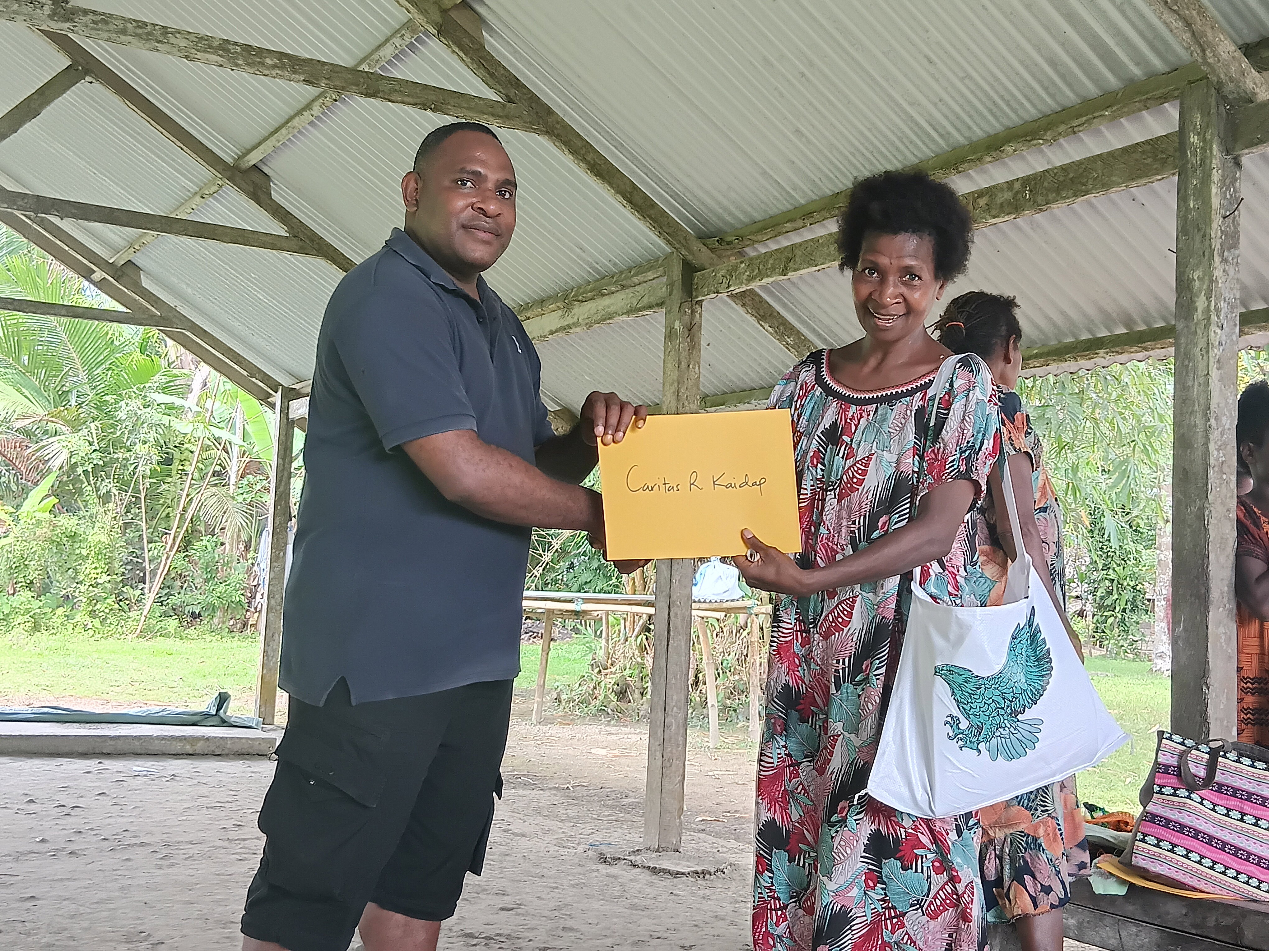 Presentation of certificate by Mr. Alwin Biari- Logistics and Security coordinator to Ms Caritas R Kaidap, one of the adult female participants.