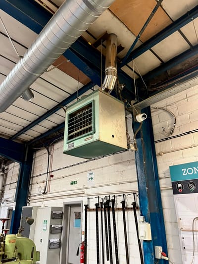 Gas-fired warm air unit heater with flue, mounted high on the wall of a workshop