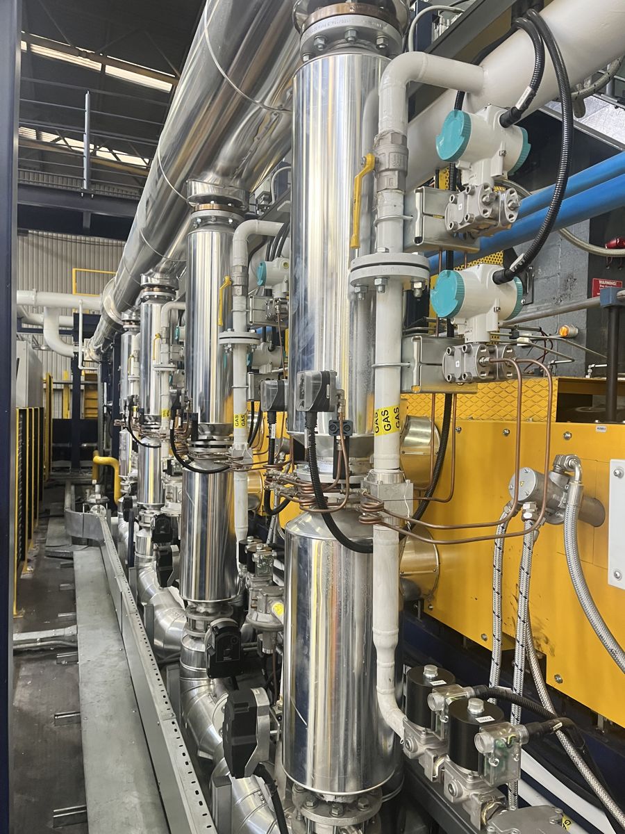 Stainless steel industrial gas train with yellow gas-labelled pipework, solenoid valves and pressure switches feeding a process burner line in a factory
