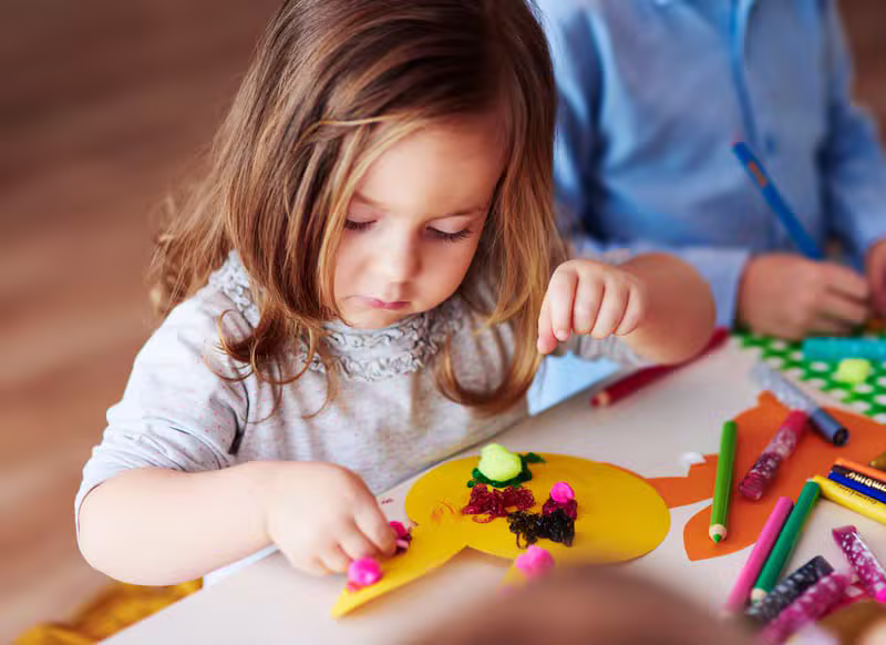 Children engaged in creative arts with an educator helping