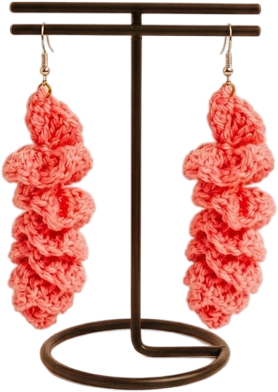 Handcrafted coral-pink ruffle crochet drop earrings displayed on a black T-bar stand against a plain white background