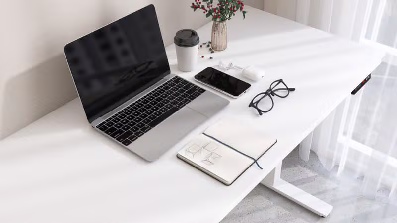 Flat lay of headphones, phone, notebook, and glasses on a light desk