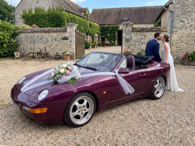Porsche cabriolet bordeaux F&F PRESTIGE décorée d’un bouquet de mariage et de tulle blanc sur le capot, devant la Ferme de la Biza à Missy-sur-Aisne