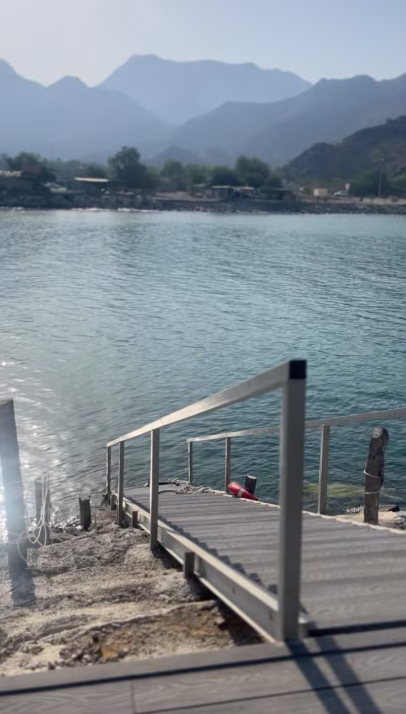 Private boat dock leading into calm sea water with mountains at Turjman Oasis Villa