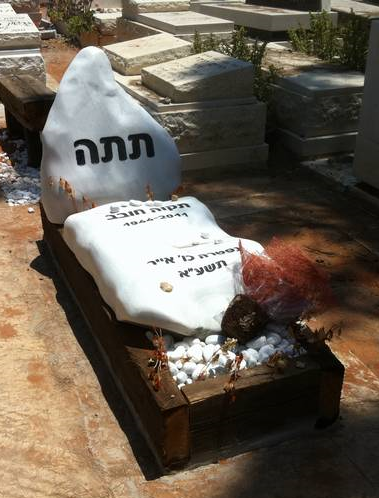 מצבה מעוצבת מאבנים לבנות המונחות על אדנית עץ חומה ליחידה