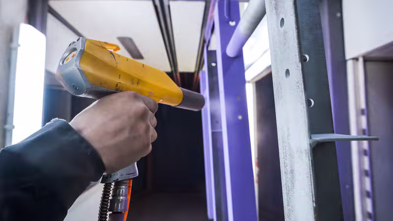 Pistolet de poudrage industriel en action sur une pièce métallique