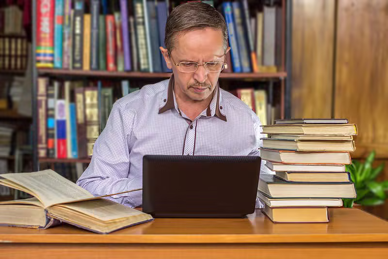 Author working on a laptop surrounded by books