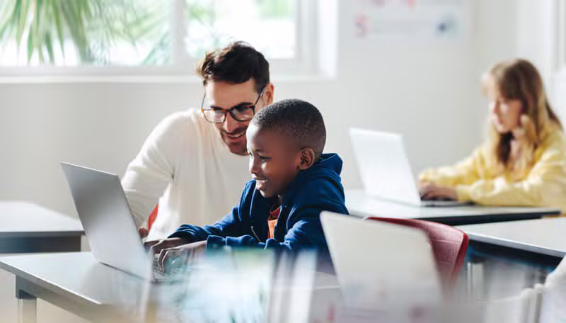 Mentor guiding young African students using a laptop