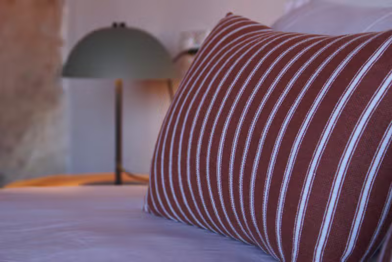 Detalle de cama acogedora con cojín y lámpara
