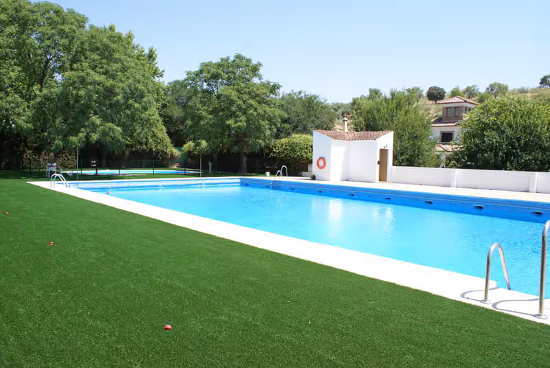 Vista amplia de la piscina municipal con césped y zona de baño