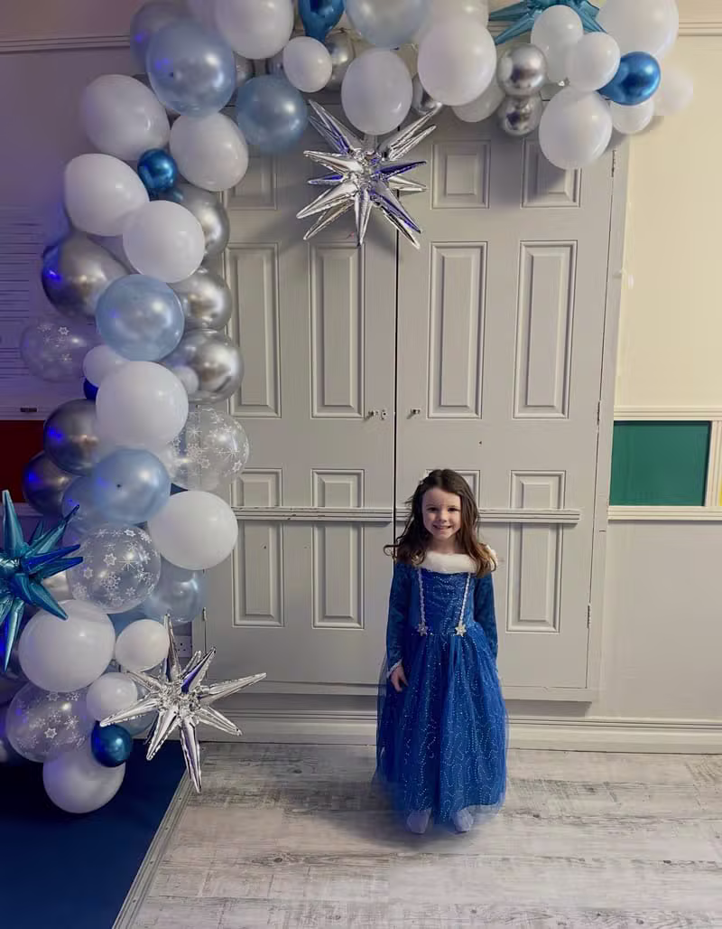 Child in a blue party dress in front of a balloon arch