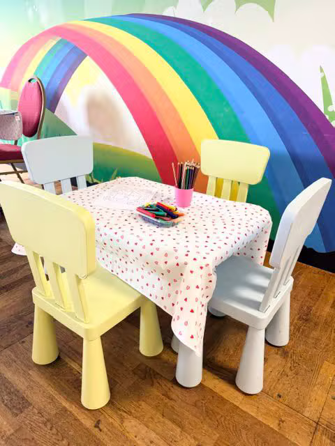 A little table and chairs set up for drawing under a rainbow wall mural