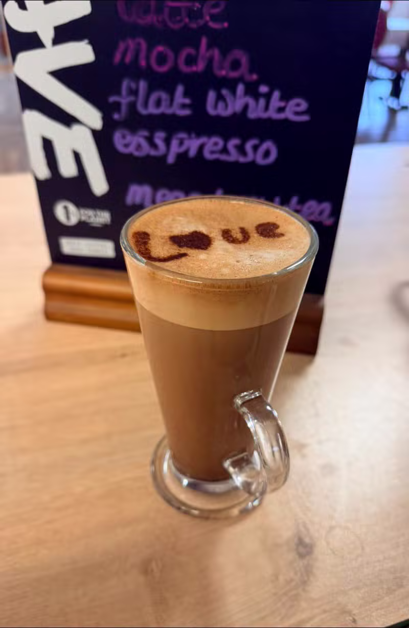 A latte in a glass mug with a hand-drawn cocoa pattern on the foam
