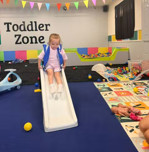 A toddler sliding down the small slide in the play area