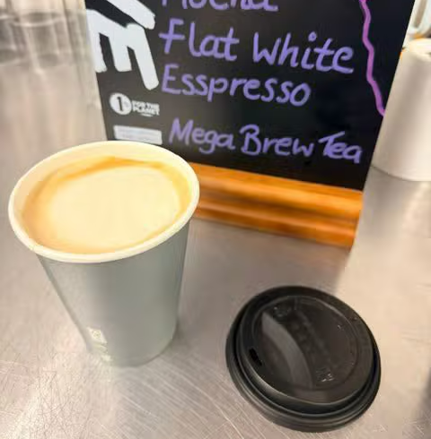 A takeaway coffee cup on a café table beside a chalkboard menu