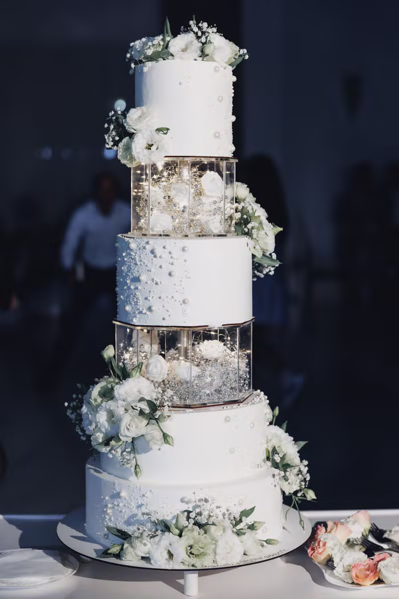 Five tier white wedding cake decorated with green and white flowers