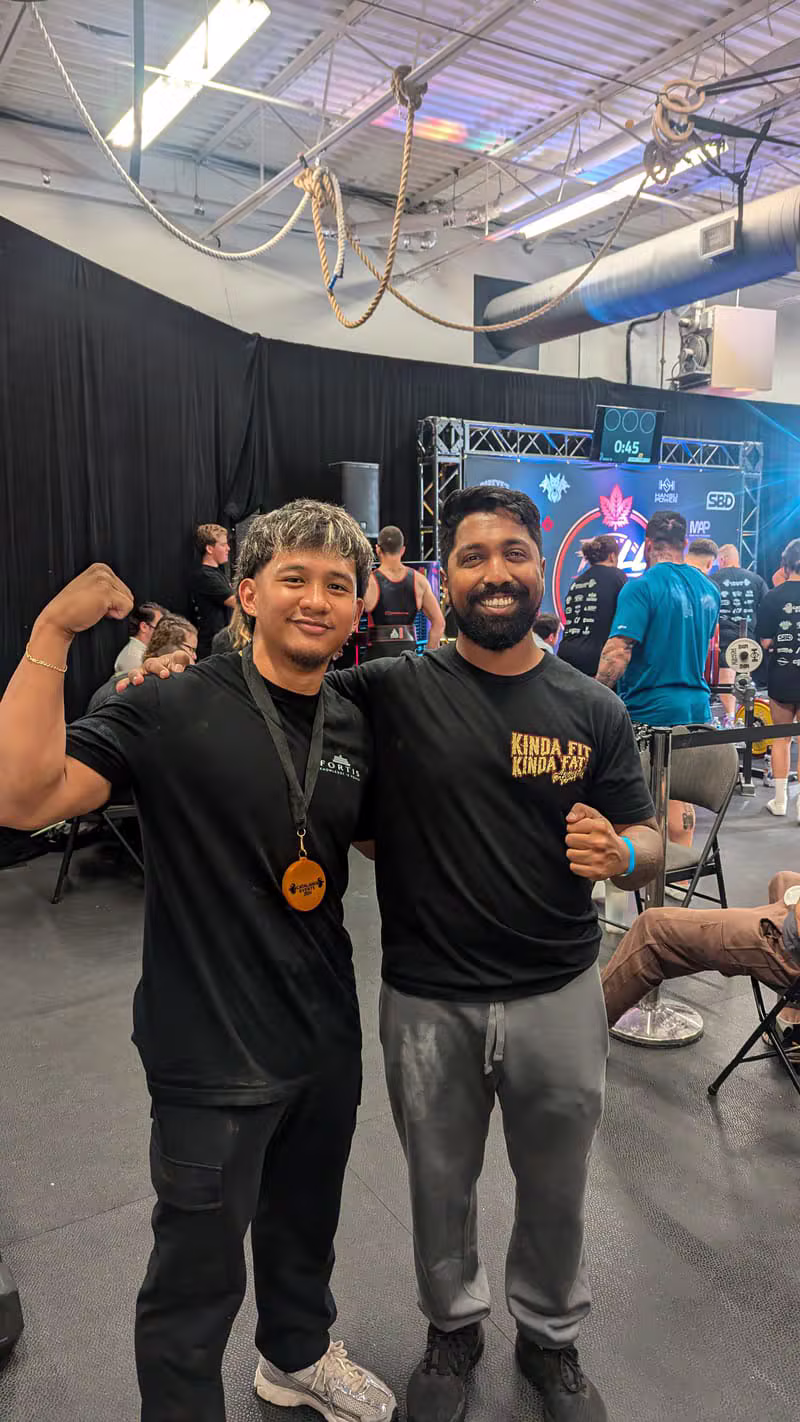 Vithusan J flexing with a training partner while wearing his competition medal at a Toronto strength event
